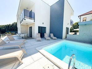 Ein moderner Poolbereich mit Liegestühlen, einem Pool und einem zweigeschossigen Gebäude mit Balkon.