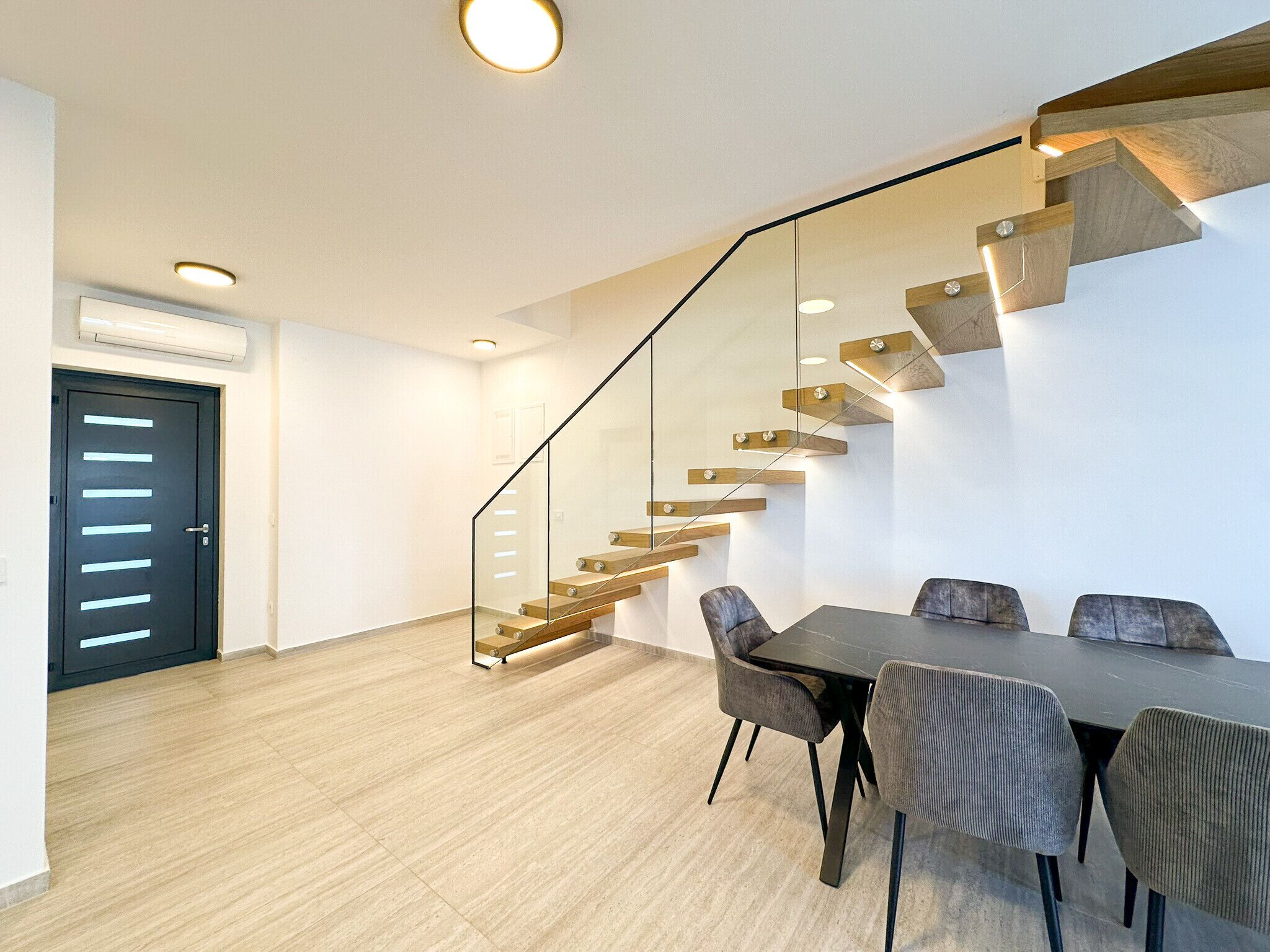 A modern interior with a staircase, a dining area, and a door.