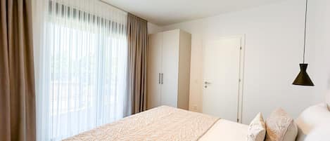 Un dormitorio con cama, cortinas, armario, puerta y una lámpara colgante.