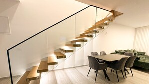 Ein modernes Interieur mit einer Holztreppe, einem Essbereich mit Stühlen und einem grünen Sofa.
