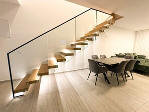 Ein modernes Interieur mit einer Holztreppe, einem Essbereich mit Stühlen und einem grünen Sofa.