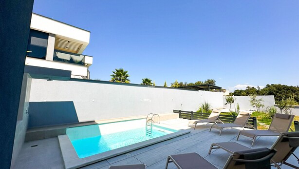 Ein moderner Poolbereich im Freien mit Liegestühlen und wolkenlosem, blauem Himmel.