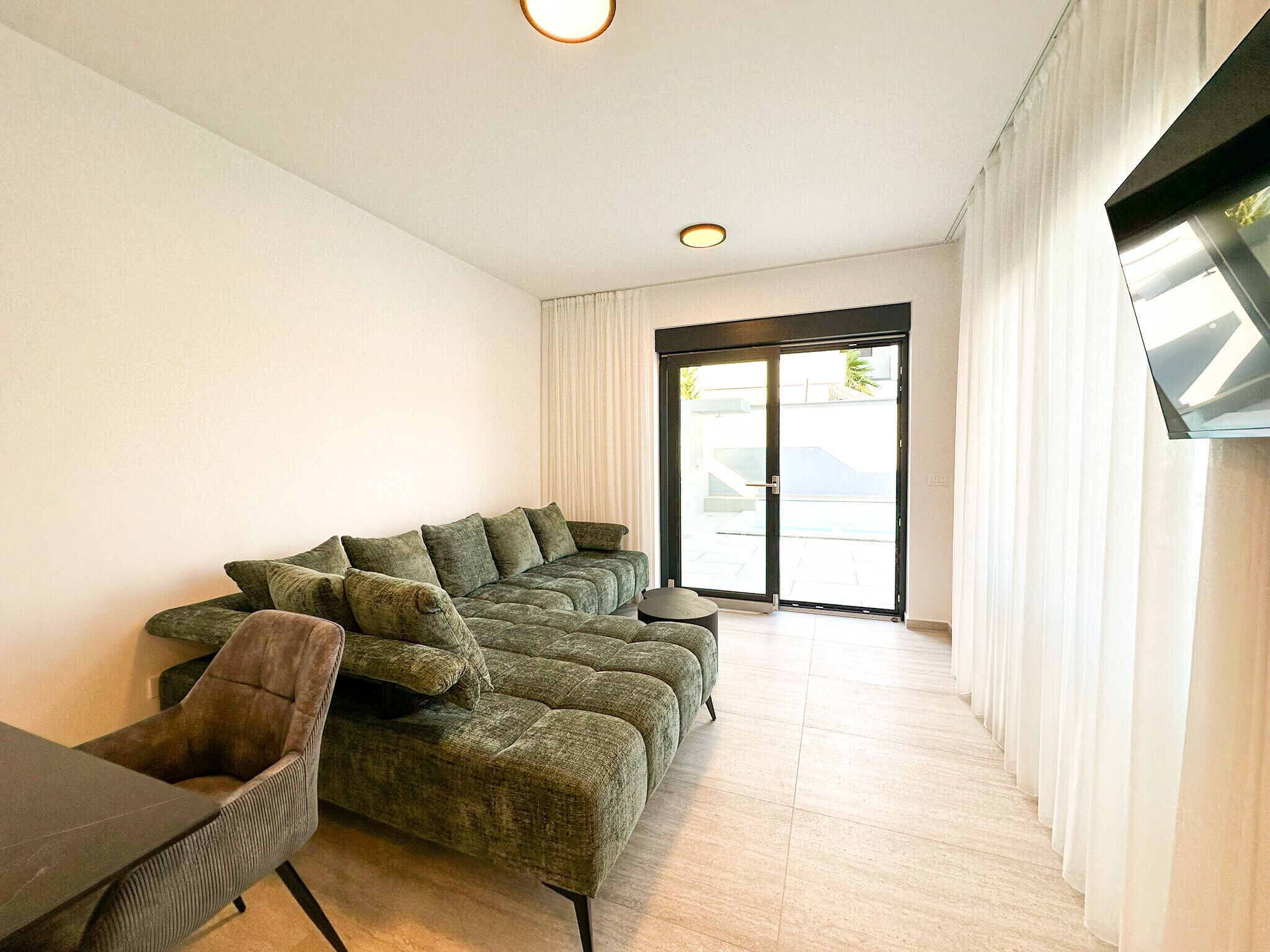 Ein modernes Wohnzimmer mit einem Ecksofa, einem kleinen runden Tisch und einem flach an der Wand befestigten Flachbildfernseher.