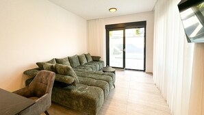Ein modernes Wohnzimmer mit einem Ecksofa, einem kleinen runden Tisch und einem flach an der Wand befestigten Flachbildfernseher.
