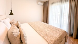 Ein Hotelzimmer mit Bett, Kissen, einer Pendelleuchte, einer Klimaanlage und einem fenster mit Vorhängen.