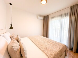 Ein Hotelzimmer mit Bett, Kissen, einer Pendelleuchte, einer Klimaanlage und einem fenster mit Vorhängen.