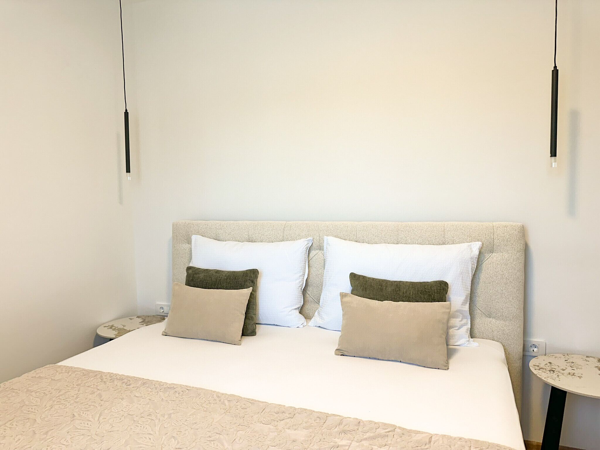 A bed with a textured headboard, two white pillows, and two beige pillows with green accents.