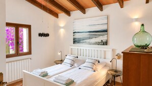 A bedroom with a bed, bedside tables, a painting, a window with flowers, and a radiator. - Canyop, 5StarsHome Villa, Mallorca (Campos)
