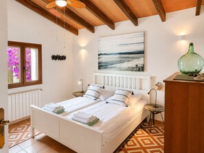 Ein Schlafzimmer mit einem Bett, Nachttischen, einem Gemälde, einem Fenster mit Blumen und einer Heizung.