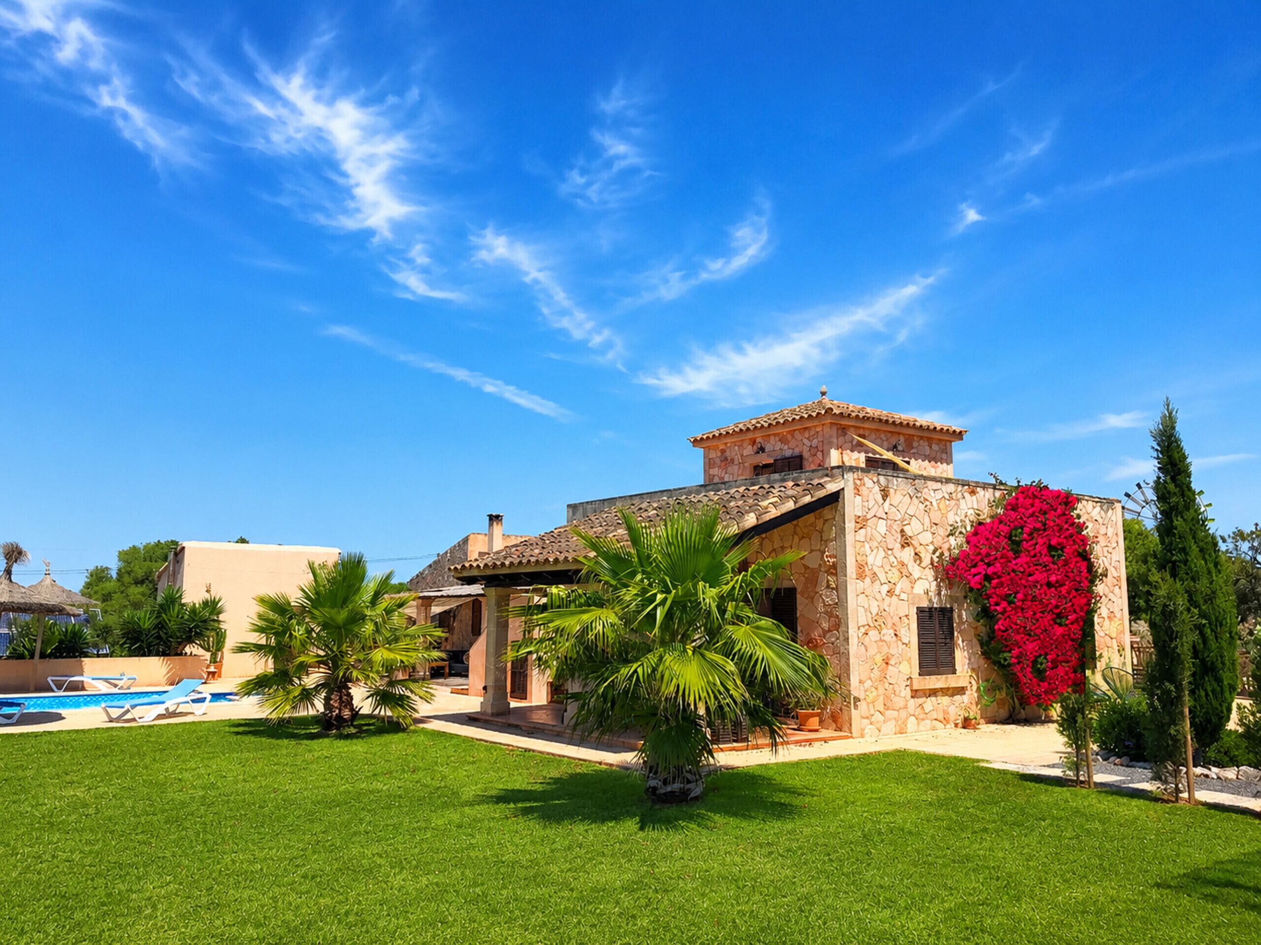 Une villa dotée d’une piscine, de palmiers et d’une façade en pierre.