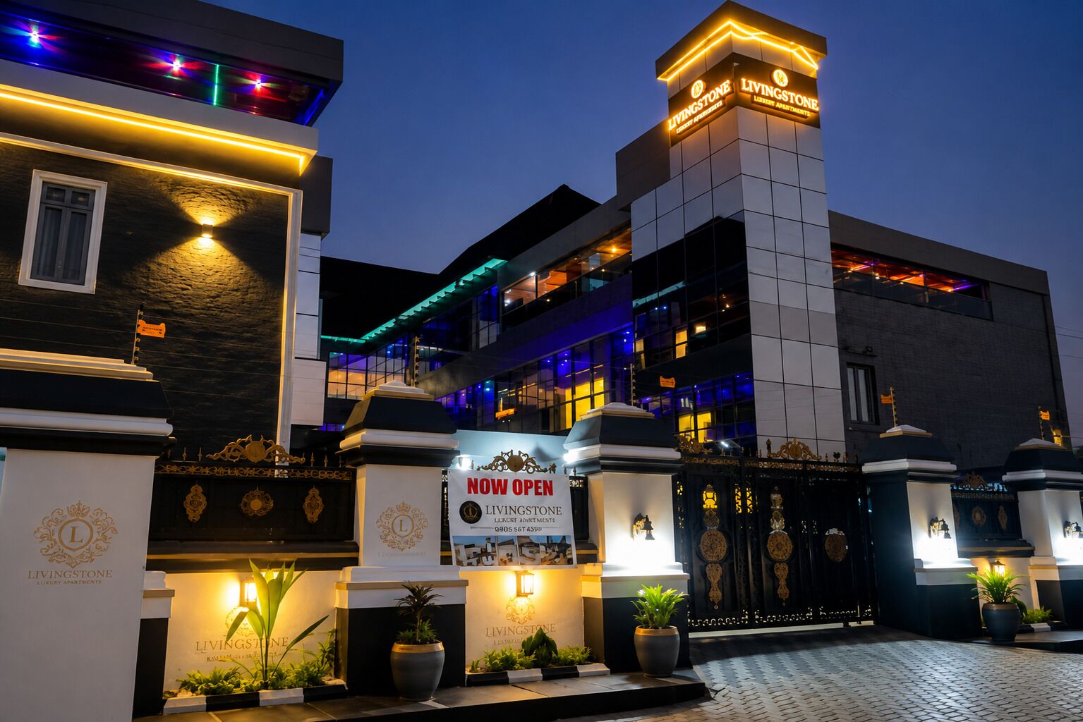 A luxury apartment building with a prominent entrance, illuminated signage, and decorative gates.