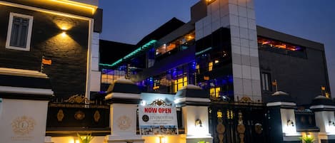 A luxury apartment building with a prominent entrance, illuminated signage, and decorative gates.
