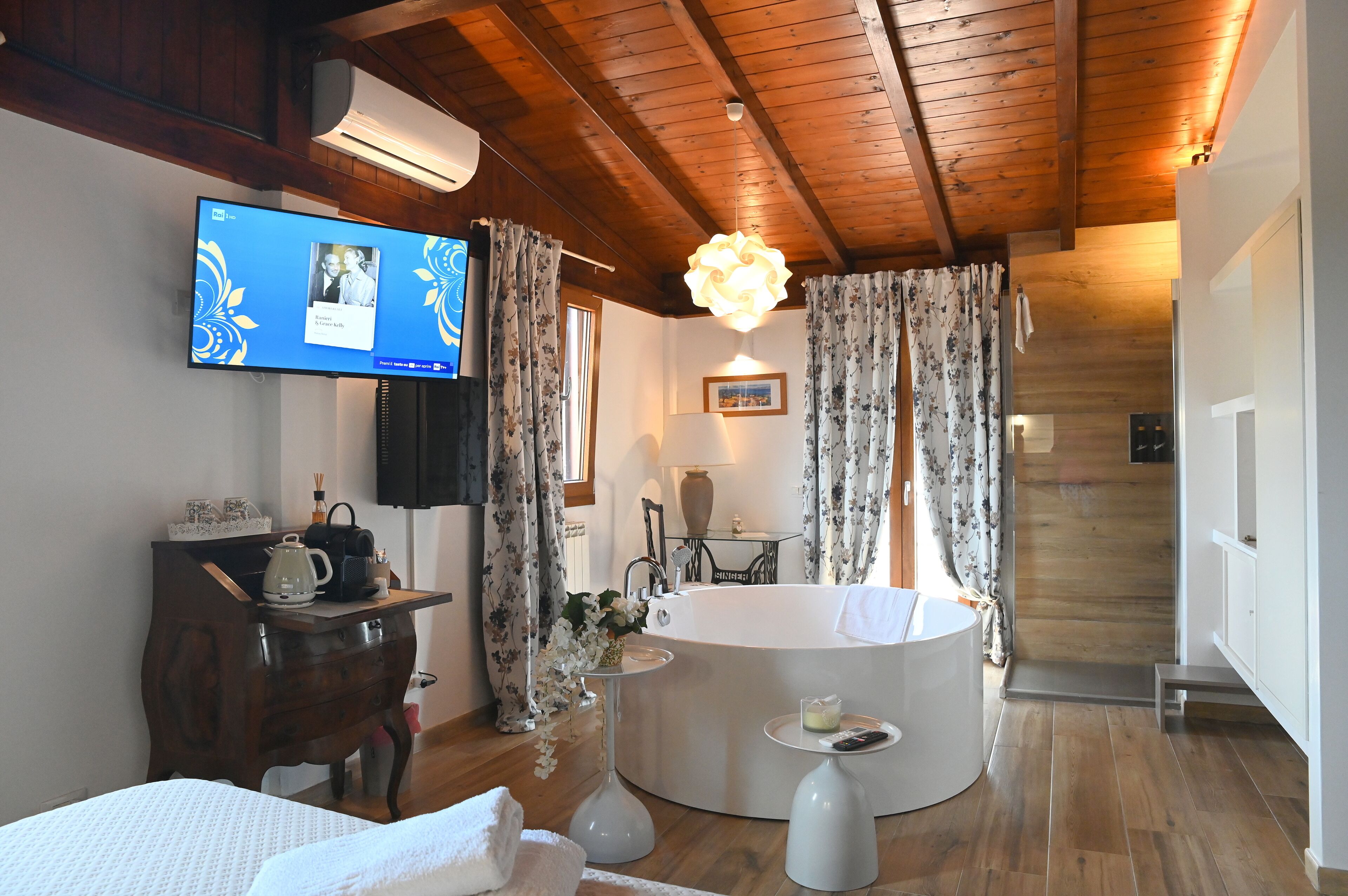 Ein Hotelzimmer mit Holzboden, einem an der Wand montierten Fernseher, einer runden Badewanne und einem kleinen Tisch mit Fernbedienung.