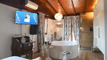 Ein Hotelzimmer mit Holzboden, einem an der Wand montierten Fernseher, einer runden Badewanne und einem kleinen Tisch mit Fernbedienung.