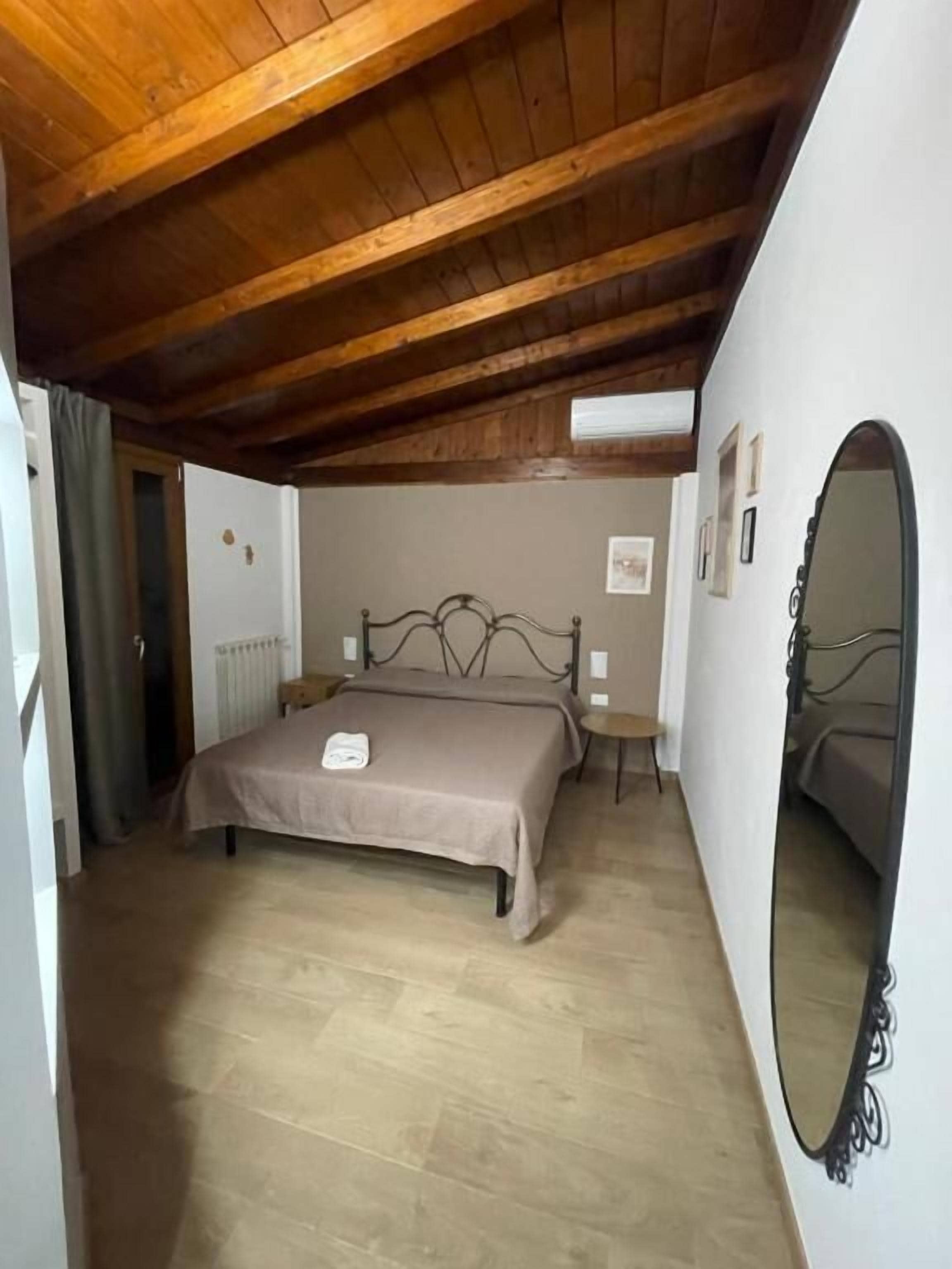 Un dormitorio con techo de madera, una cama con cabecera, un espejo redondo y un radiador.