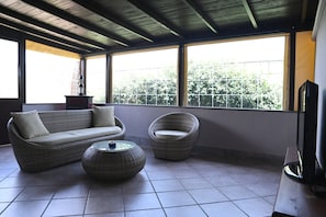 A room with a sofa, two chairs, a small table, and a television.