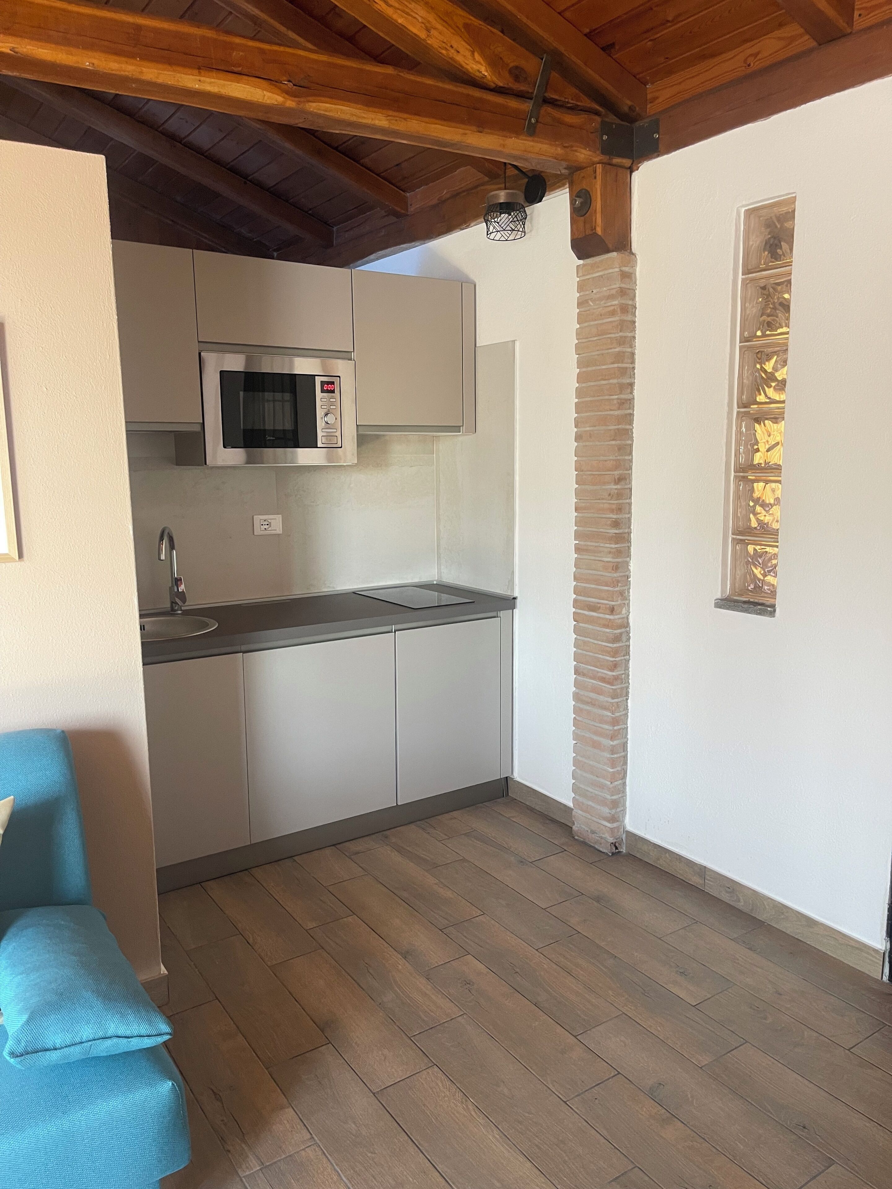 Una cucina compatta con forno a microonde, lavandino e pavimento in legno.