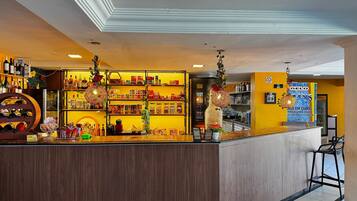 Área de bar com prateleiras repletas de garrafas e petiscos, balcão com caixa registradora e luminárias decorativas penduradas.