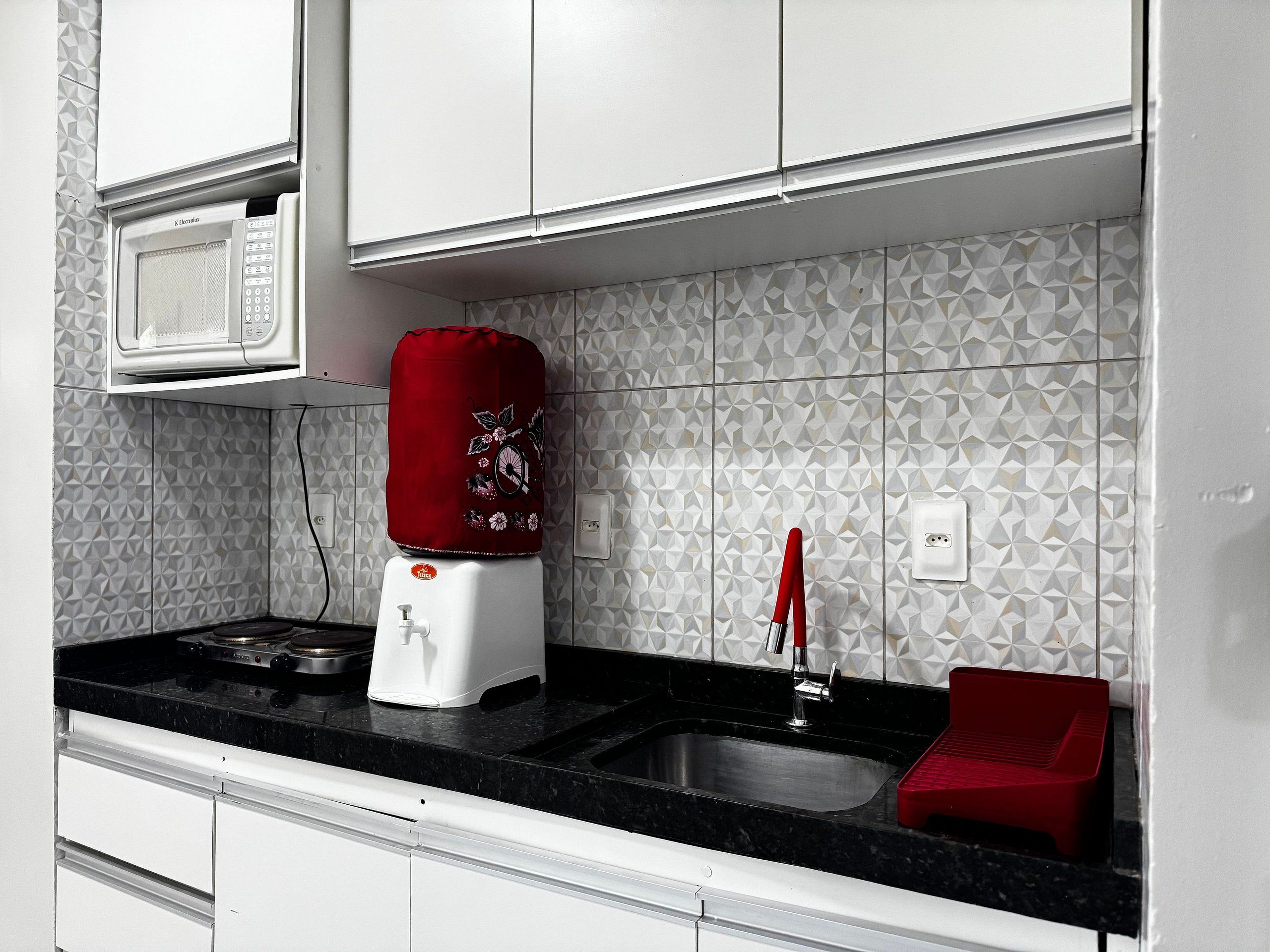 Cozinha com micro-ondas, um dispensador de água vermelho, pia e escorredor de louça vermelho.