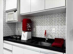 A kitchen with a microwave, a red water dispenser, a sink, and a red dish rack.