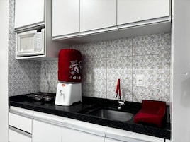 Una cocina con microondas, dispensador de agua rojo, pileta y escurridor rojo.
