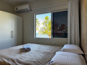 A bedroom with a bed, a window with a view of palm trees, and an air conditioning unit.