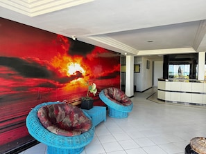 A lobby with a large wall mural, two blue wicker sofas, a reception desk, and a tiled floor. - Apart Hotel Marinas Tamandaré Carneiros (Praia dos Carneiros)