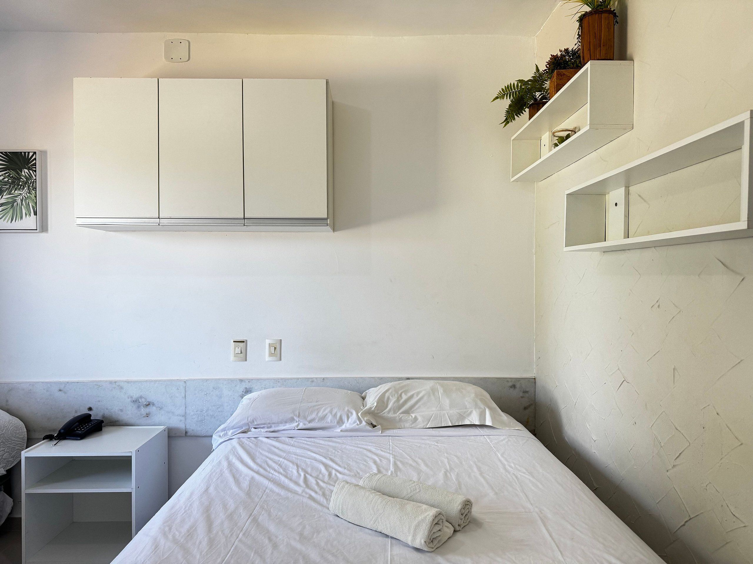 A bedroom with a bed, a nightstand, a wardrobe, and built-in shelving with plants.