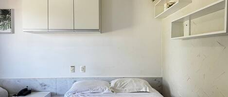 A bedroom with a bed, a nightstand, a wardrobe, and built-in shelving with plants.