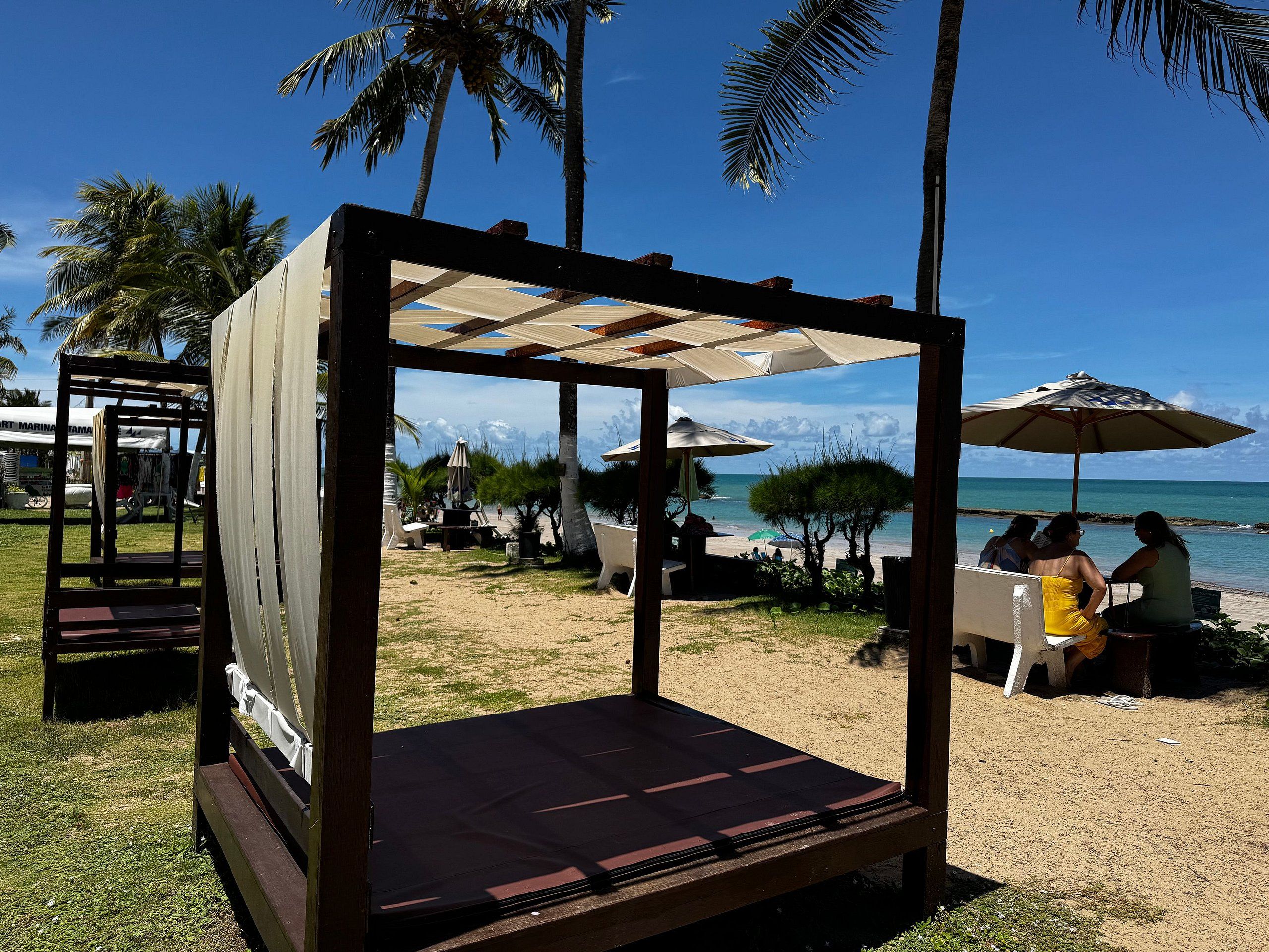 Un área de estar frente a la playa con estructura de madera, sombrillas y vista al océano.