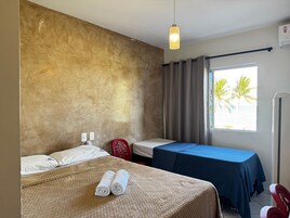 Quarto de hotel com cama, escrivaninha, cadeira e janela com cortinas.
