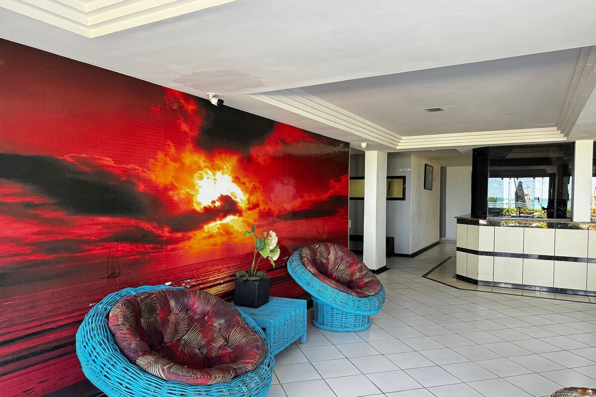 A lobby with a large wall mural, two blue wicker sofas, a reception desk, and a tiled floor.