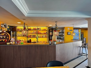 A bar area with shelves stocked with bottles and snacks, a counter with a cash register, and hanging decorative lights.