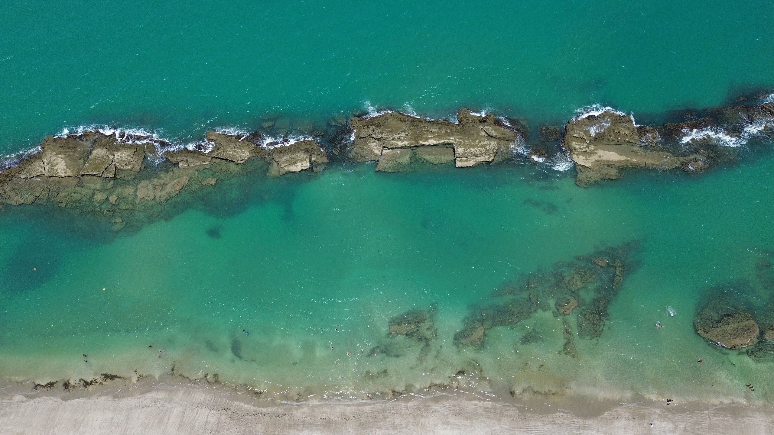 Un paisaje costero con aguas turquesas cristalinas, formaciones rocosas y una playa de arena.
