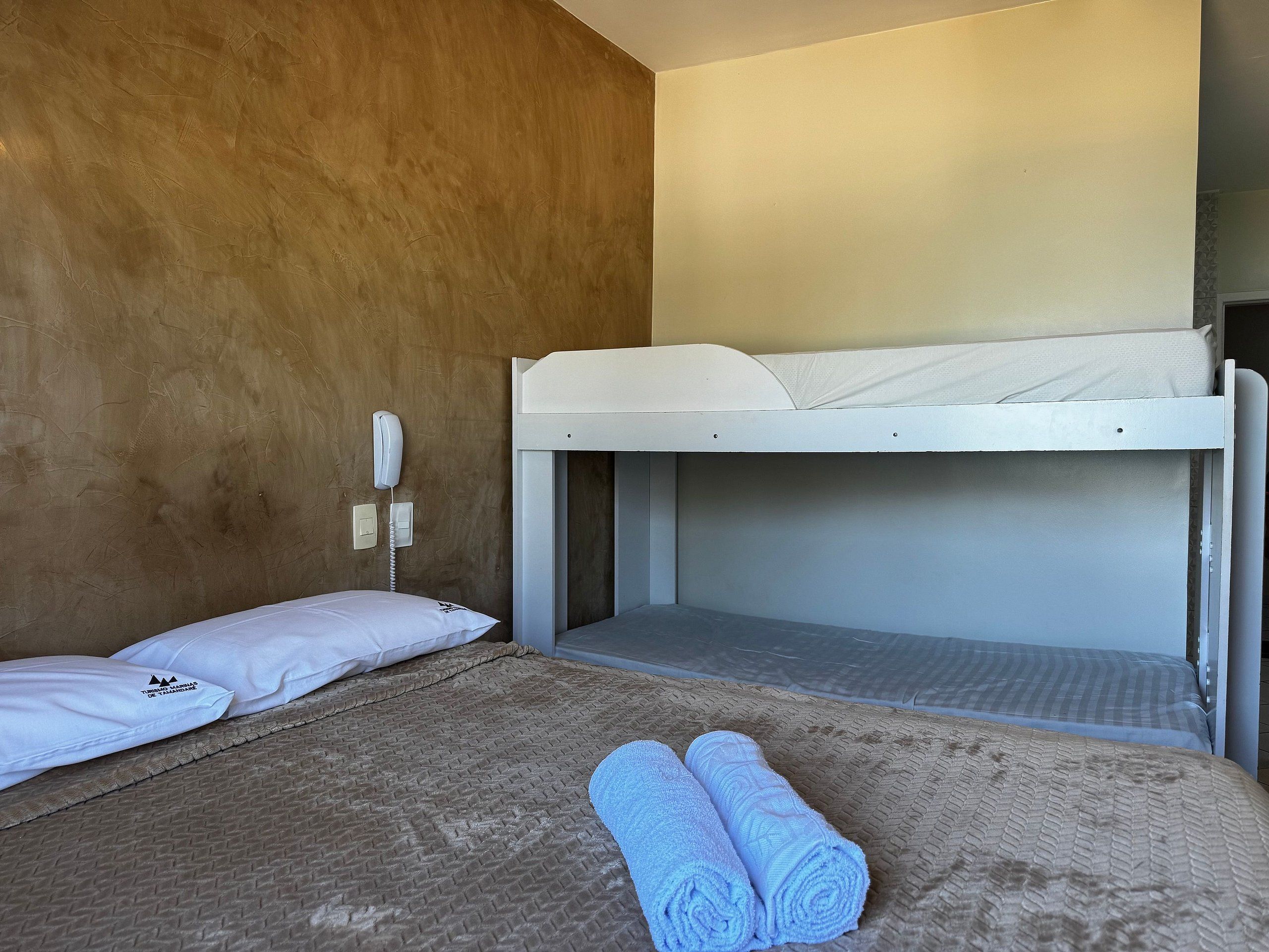 Una cama litera con un colchón blanco, una colcha marrón con textura y dos toallas enrolladas en la litera inferior.