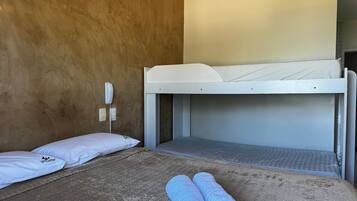 Una cama litera con un colchón blanco, una colcha marrón con textura y dos toallas enrolladas en la litera inferior.