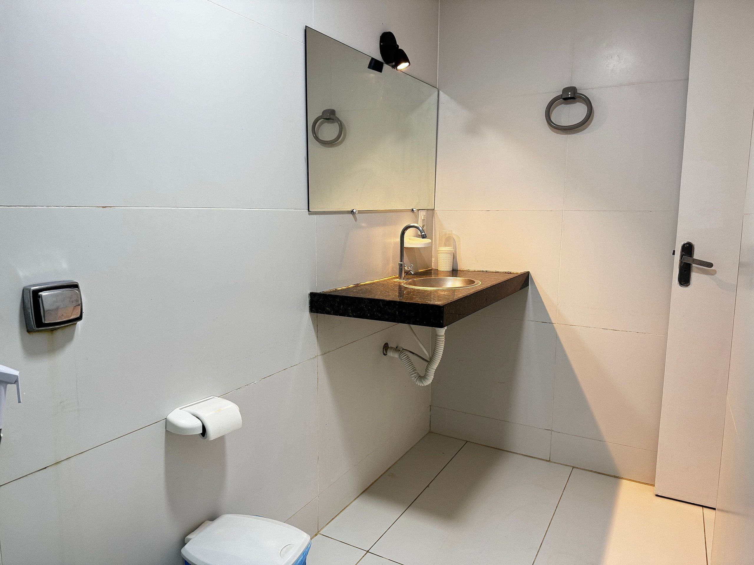Casa de banho com sanita, lavatório, espelho, suporte para toalhas e dispensador de papel.
