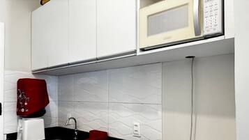 Cozinha com micro-ondas, cafeteira vermelha e fogão elétrico de duas bocas.