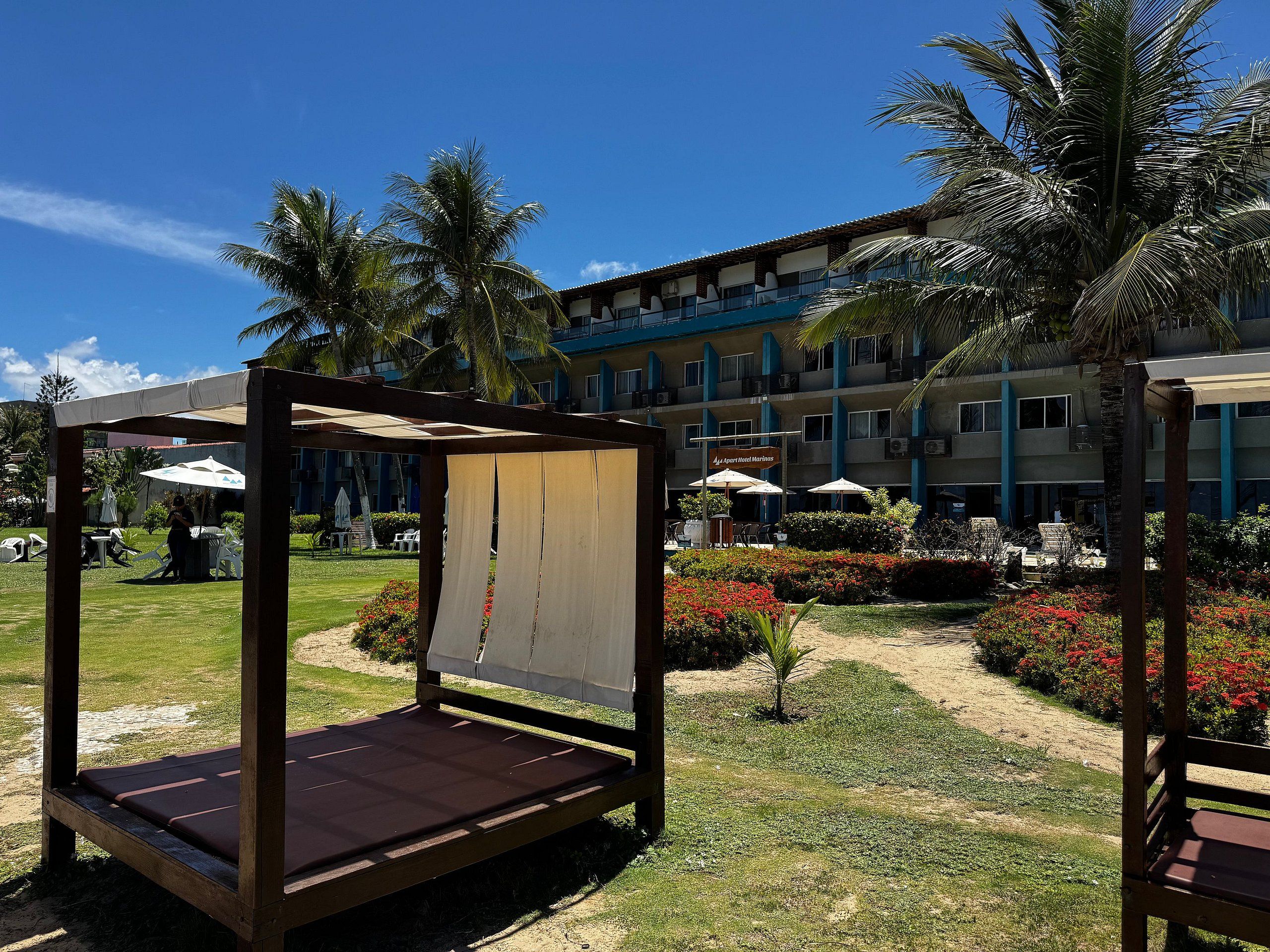 Um hotel com área de piscina, mobiliário de jardim e um jardim de palmeiras.