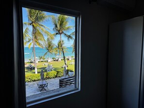 A window view of a beachside area with palm trees and outdoor seating.