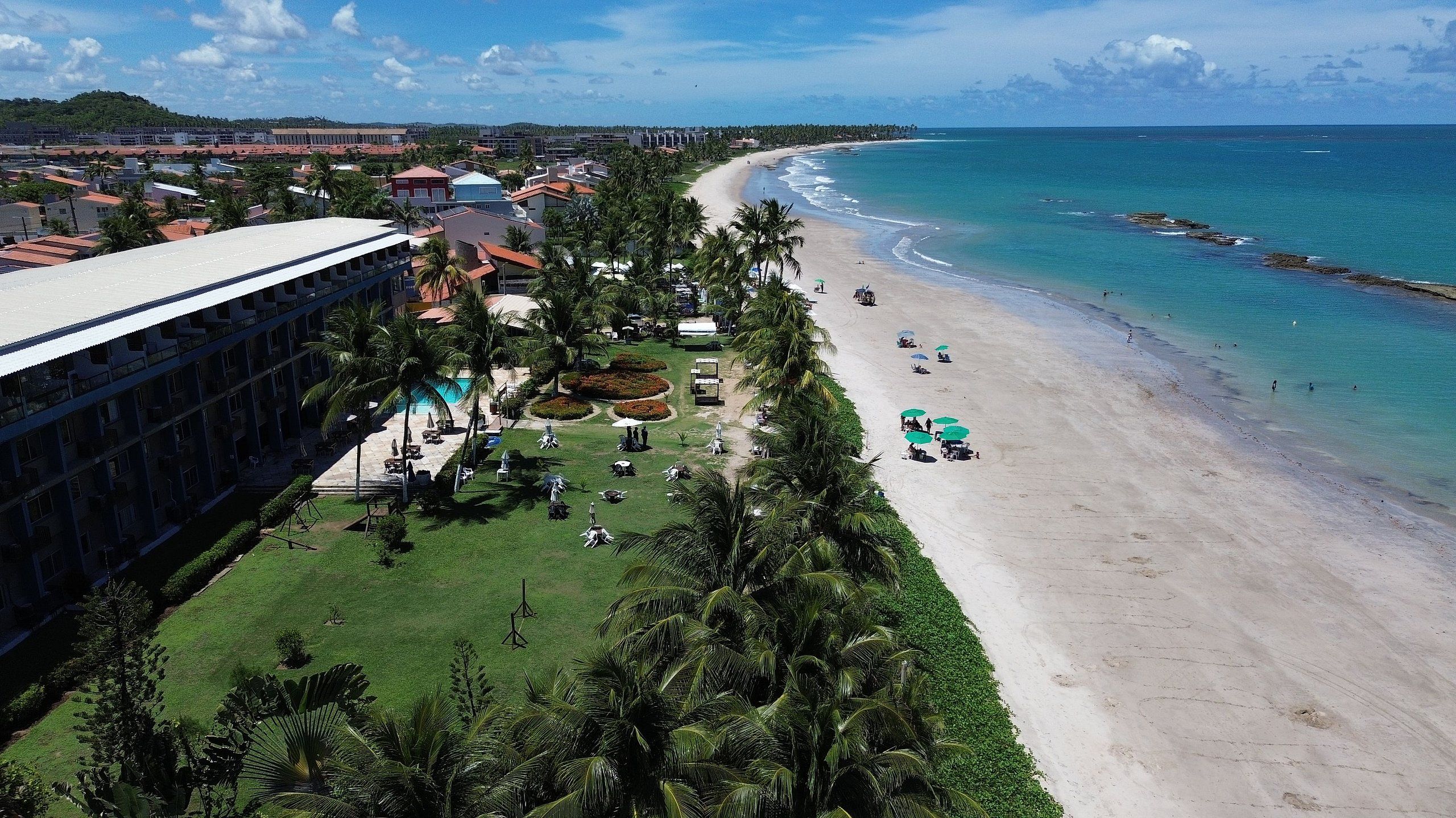 Hotel à beira-mar com praia, piscina e vegetação exuberante.