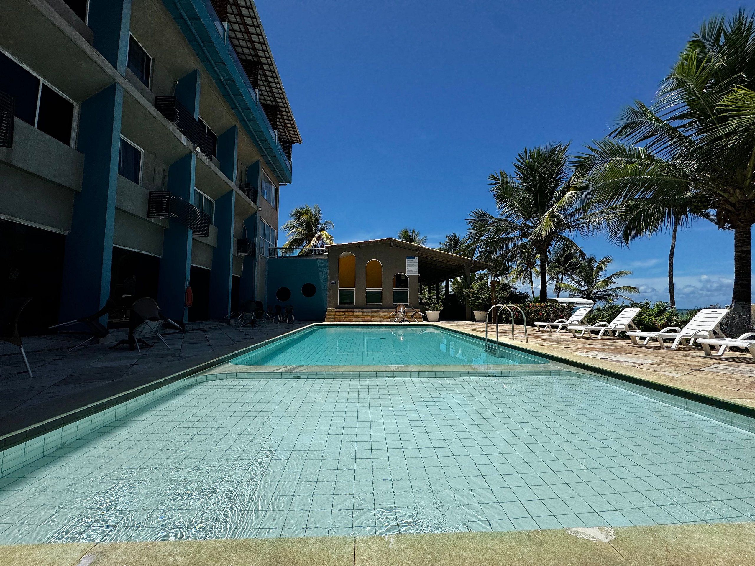 Una piscina con sillas de descanso y un edificio con varios balcones.