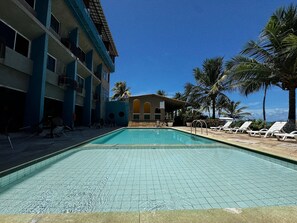 A swimming pool with lounge chairs and a building with multiple balconies.