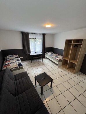 A compact living space with a sofa, a small table, a bed, a desk, and a wardrobe.