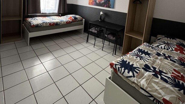 Ein Zimmer mit einem Bett, einem Schreibtisch und einem Kleiderschrank.