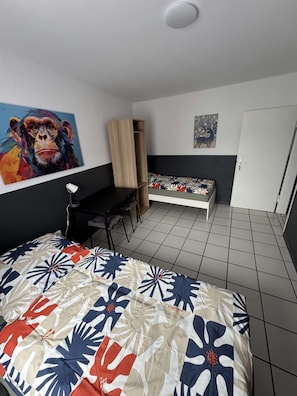 A room with a bed, a desk, a chair, and a wall with a painting.