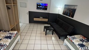Ein kompakter Wohnbereich mit einer Couch, einem an der Wand befestigten Fernseher, einem kleinen Tisch und einer Essecke mit Stühlen.