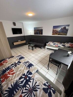 A hotel room with a bed, a sofa, a small table, a TV mounted on the wall, and two paintings.