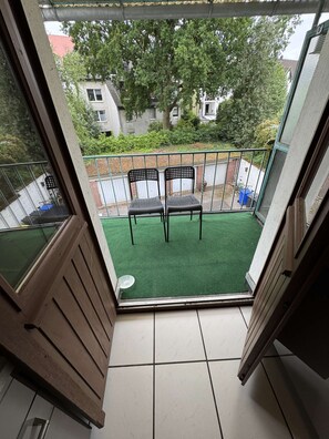 Ein Balkon mit zwei Stühlen, einem grünen Kunstrasen und Blick auf die Nachbarschaft.