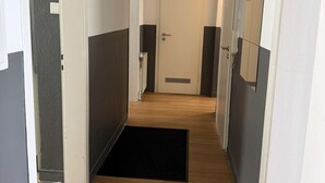 Un passadís amb sòl de fusta, un estri de fusta, una porta blanca i un quadre amb marc negre a la paret.